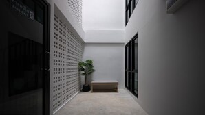 A narrow hallway with a bench, a potted plant, and a fire exit sign. - Chamemon Bed Phuket Town (Phuket)
