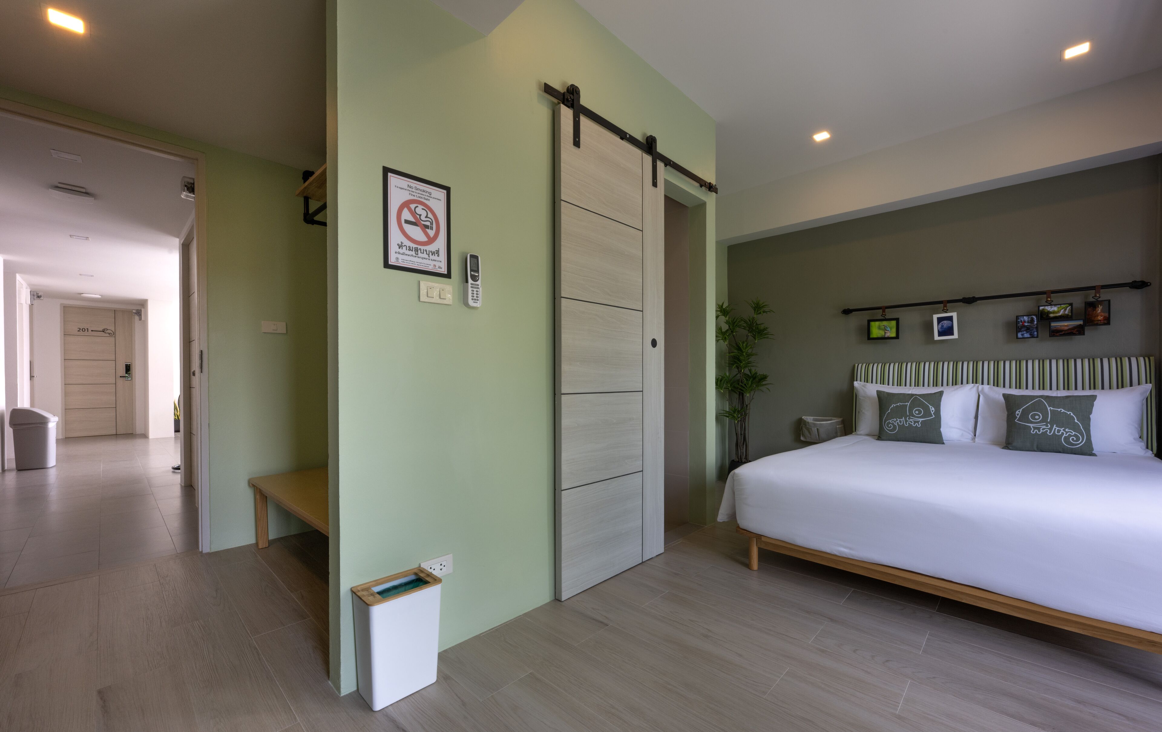 Een moderne hotelkamer met een bed, een schuifdeur, een bankje, een prullenbak en een aan de muur bevestigd telefoon.