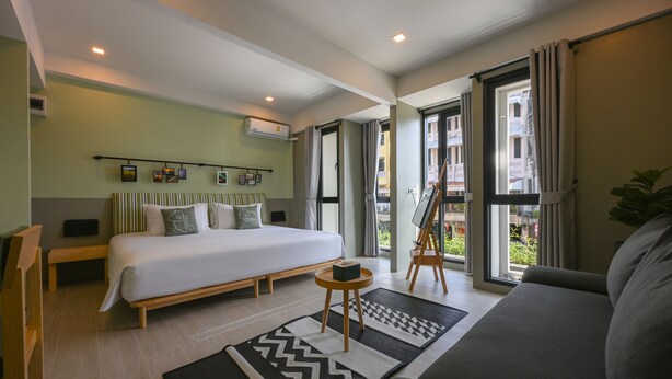 A modern hotel room with a large bed, a sofa, a small table, and a painting on easel. - Chamemon Bed Phuket Town (Phuket)
