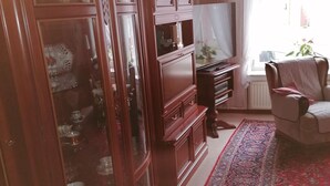 Un salón tradicional con un mueble grande de madera, un televisor, una alfombra estampada y una ventana con cortinas.