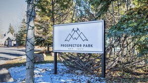 A sign for Prospector Park with a mountain logo, established in 1977, surrounded by trees and snow.