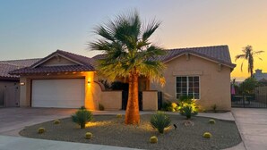 Une maison de plain-pied avec un garage, un jardin bien entretenu avec des cactus et un palmier.
