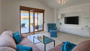A spacious living room with a sofa, a glass coffee table, and a blue armchair.