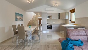 A modern kitchen with a dining area, a staircase, and a living room with a sofa.