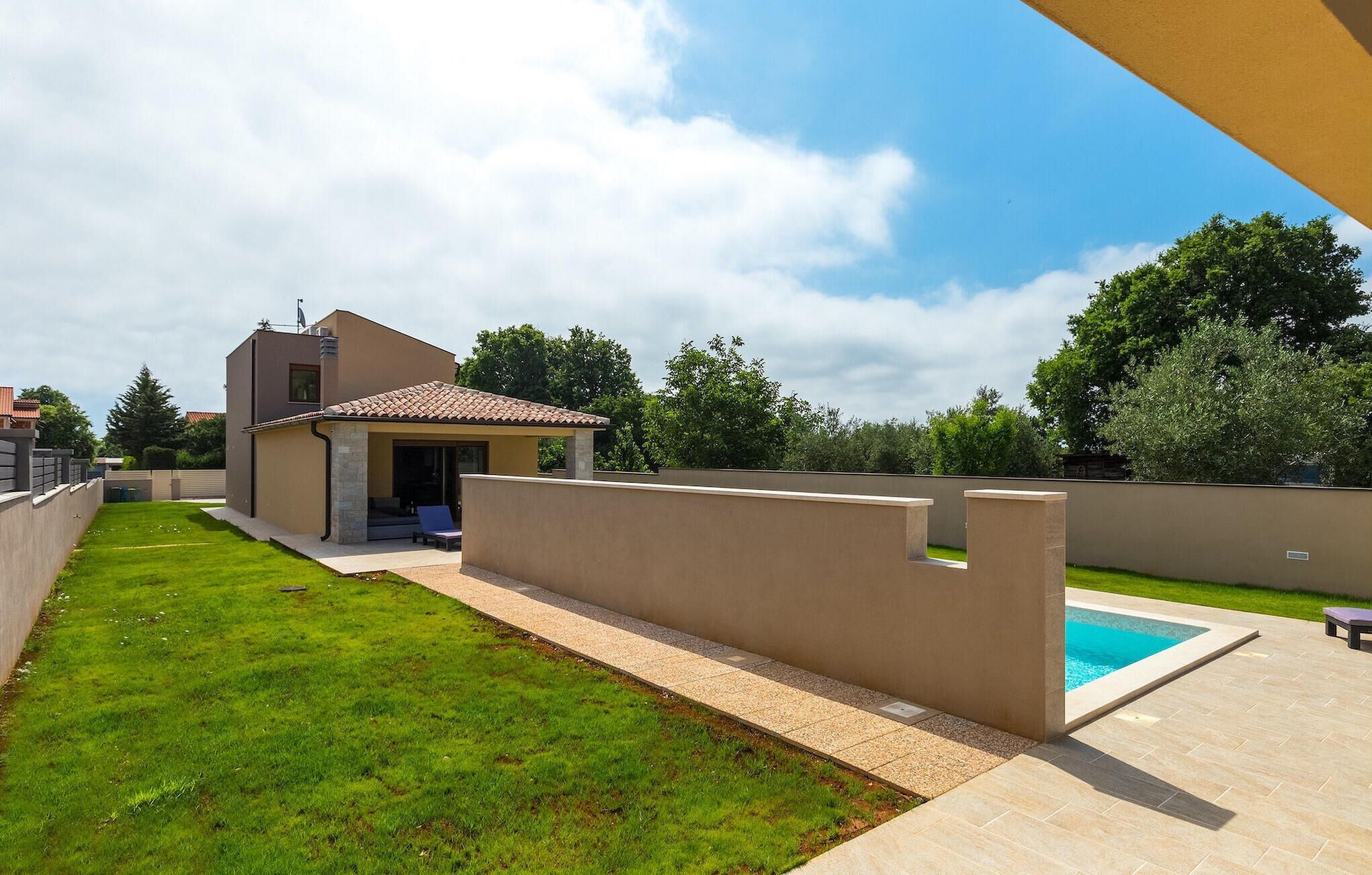 Ein modernes Haus mit Terrasse, Pool und gepflegtem Rasen.