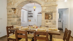 Un espace repas agrémenté d’une arche en pierre, d’un lustre et d’une cuisine visible à travers l’arche.