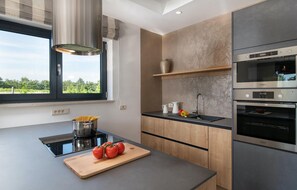 Eine moderne Küche mit Einbauherd, einem großen Fenster und Blick ins Grüne.