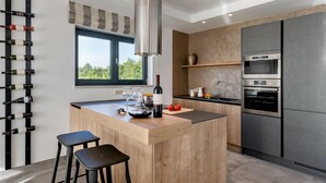 A modern kitchen with a central island, bar stools, a wine rack, and a large window. - Awesome home in Svetvincenat (Svetvincenat)