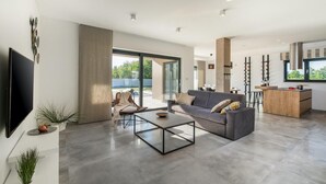 A modern living room with a grey sofa, a glass coffee table, and a TV mounted on the wall. - Awesome home in Svetvincenat (Svetvincenat)