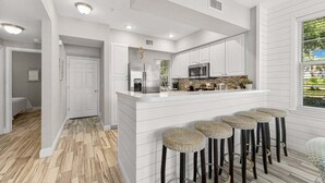 A modern kitchen with white cabinetry, a central island with bar stools, and a large window with a view.