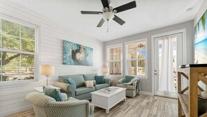 A living room with a white ceiling fan, a green sofa set, a white coffee table, and a patterned armchair.
