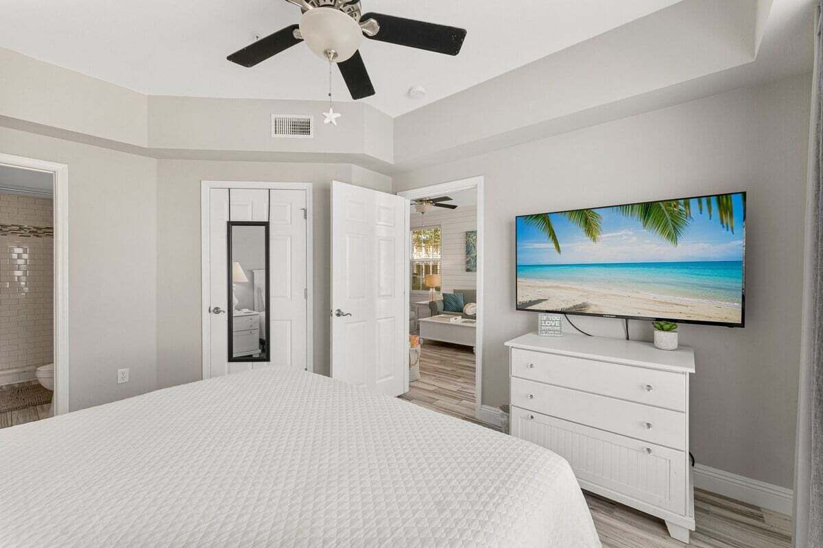 Een slaapkamer met een bed, een plafondventilator, een televisie aan de muur en uitzicht op het strand.