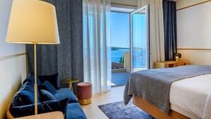 A modern hotel room with a bed, a sofa, a lamp, and a view of the sea through large windows. - New Villa/Amazing sea views/close to City and Beach/Heated pool/Sauna/Gym (Hvar)