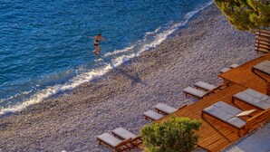 A pebbled beach with wooden lounge chairs and a person running along the water's edge. - New Villa/Amazing sea views/close to City and Beach/Heated pool/Sauna/Gym (Hvar)