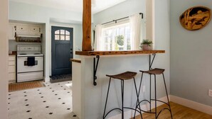 A kitchen with a white stove, a blue door, and a wooden bar counter with stools.