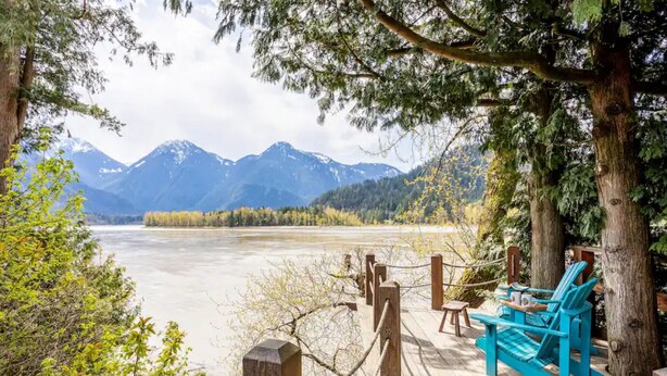 A wooden deck with chairs overlooking a river and mountains.