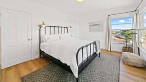 A bedroom with a bed, a window with a view, a door, and a ceiling light. - Casa Aurelia by Oraklus (Malibu)