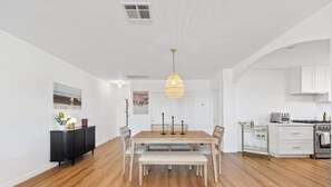 A modern kitchen with white cabinets, a dining area with a wooden table and bench, and a hanging pendant light. - Casa Aurelia by Oraklus (Malibu)
