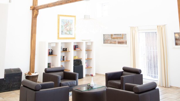 Une pièce spacieuse avec un plafond haut soutenu par des poutres en bois, une cheminée et un coin salon comprenant des canapés et une table basse.