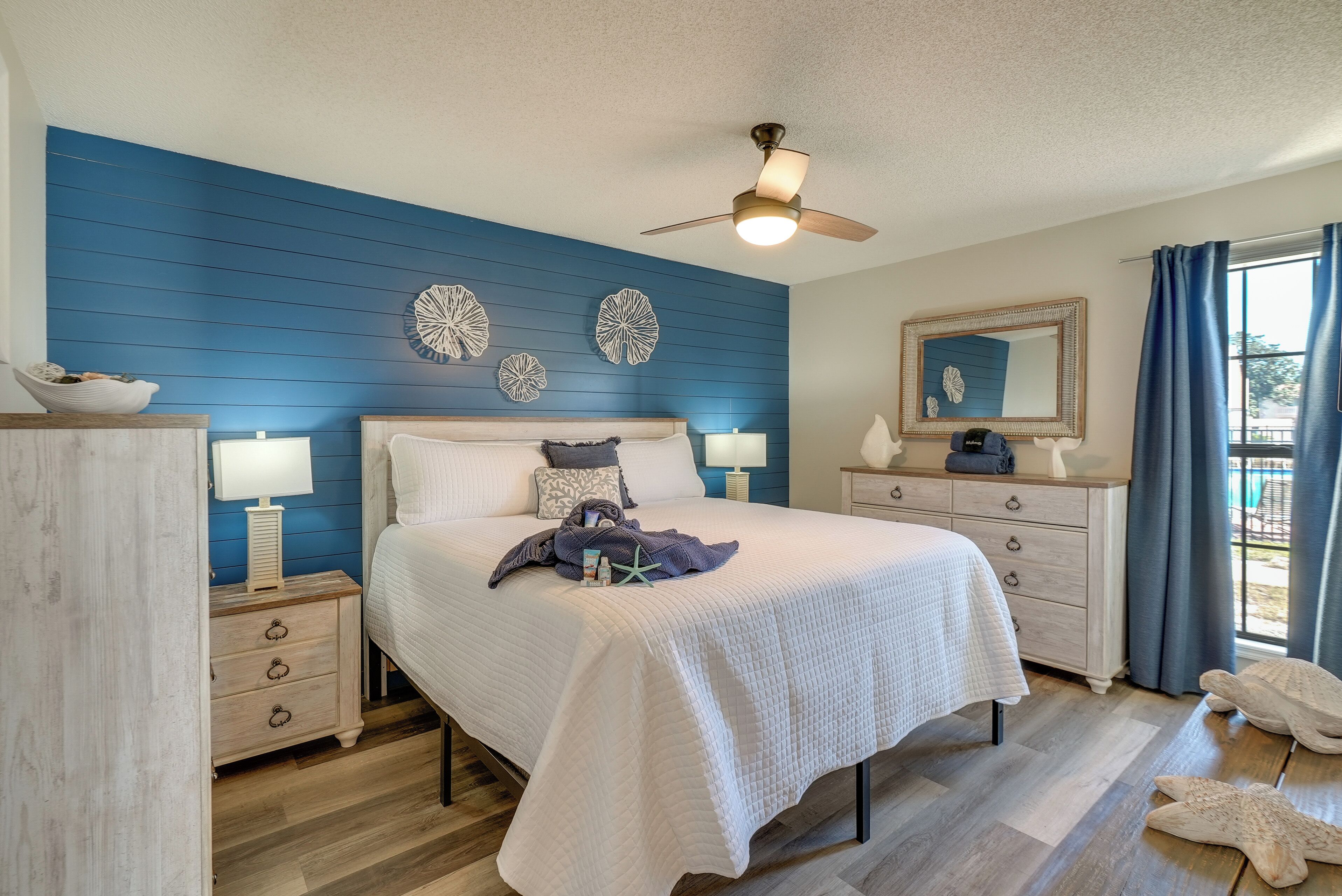 A bedroom with a bed, nightstands, a dresser, a ceiling fan, and decorative wall art.
