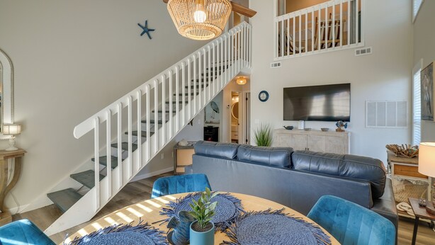 A modern living room with a staircase, blue furniture, and a large TV.
