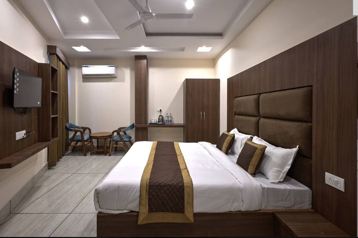 A hotel room with a bed, a desk, a chair, an air conditioning unit, and a television.