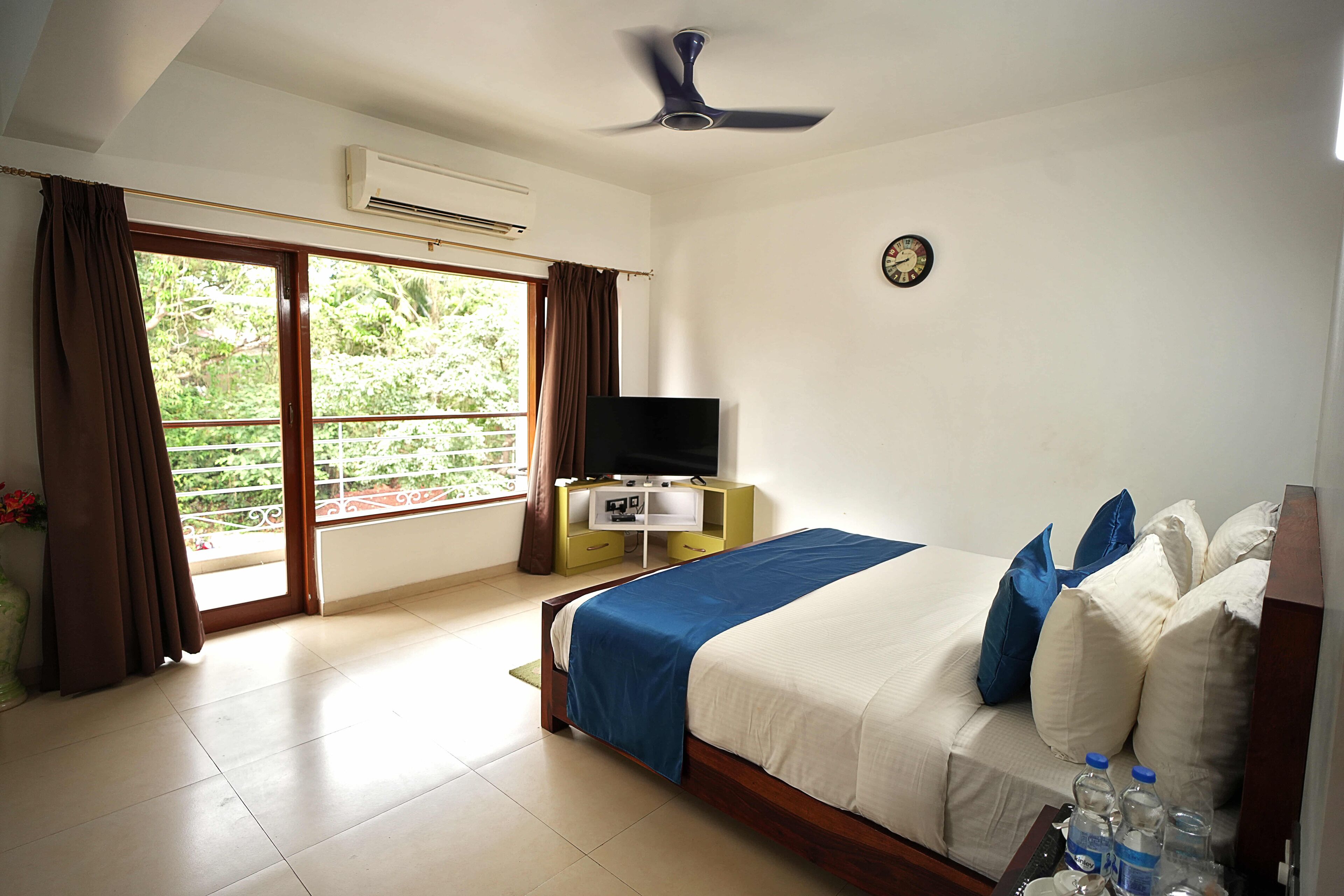 A hotel room with a bed, a TV, a desk, and a balcony with curtains.