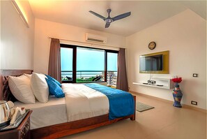 A hotel room with a bed, a ceiling fan, a TV, a vase with flowers, and a view of the sea. - Rio Grand A Premium Hotel (Haridwar)
