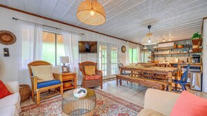 A spacious living area with a large dining table, wicker furniture, and a television mounted on the wall.