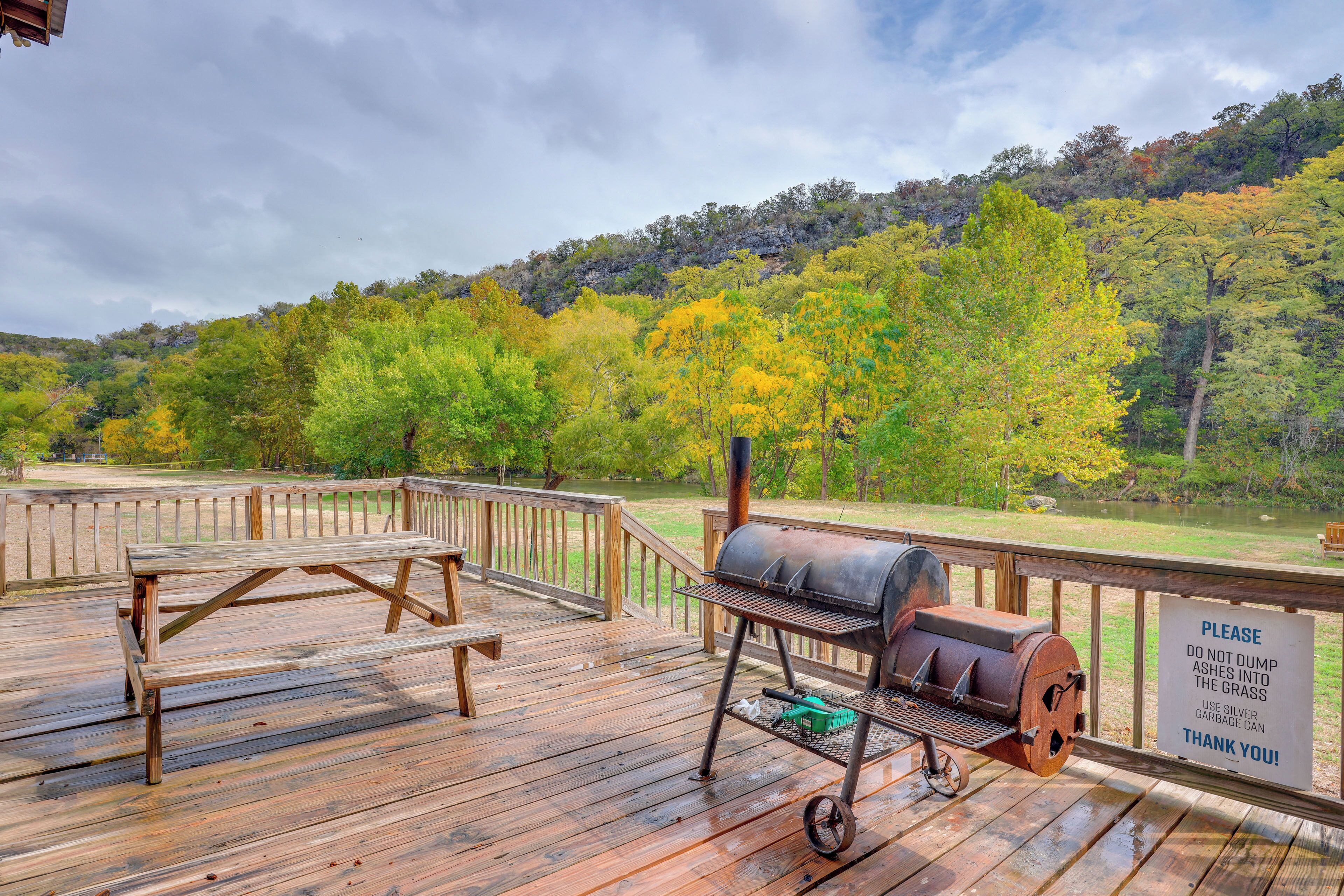 A wooden deck with a barbecue grill and picnic table, overlooking a forested area.