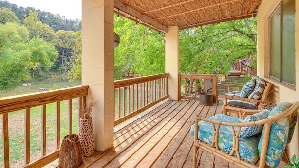 A wooden deck with a railing, wicker furniture, and a view of a river and trees.