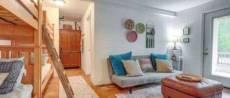 Une pièce chaleureuse avec un lit superposé, un canapé, un pouf en cuir et une table à manger.