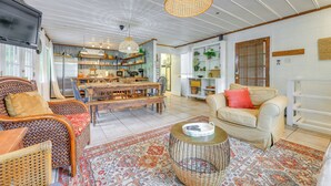 A spacious living room with a large wooden dining table, wicker furniture, and a cozy sofa.