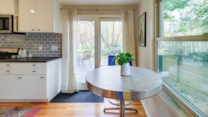 Een moderne keuken met witte kastjes, een grijze spatwand en een ronde tafel met een plant.