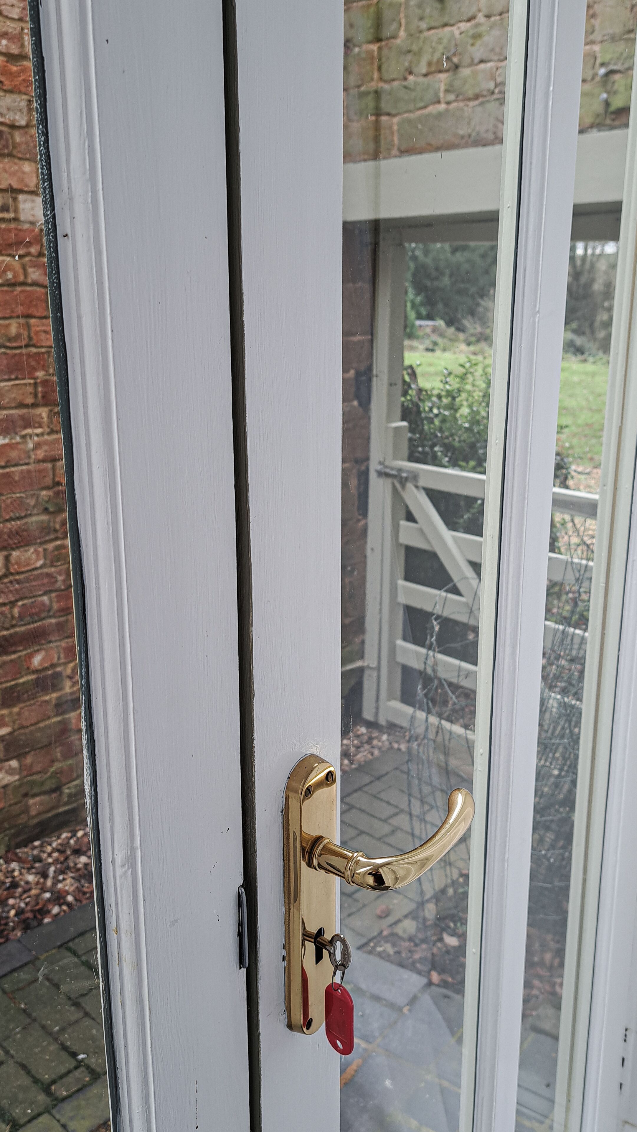 A door with a brass handle and a keyhole, leading to a brick wall and a glass door.