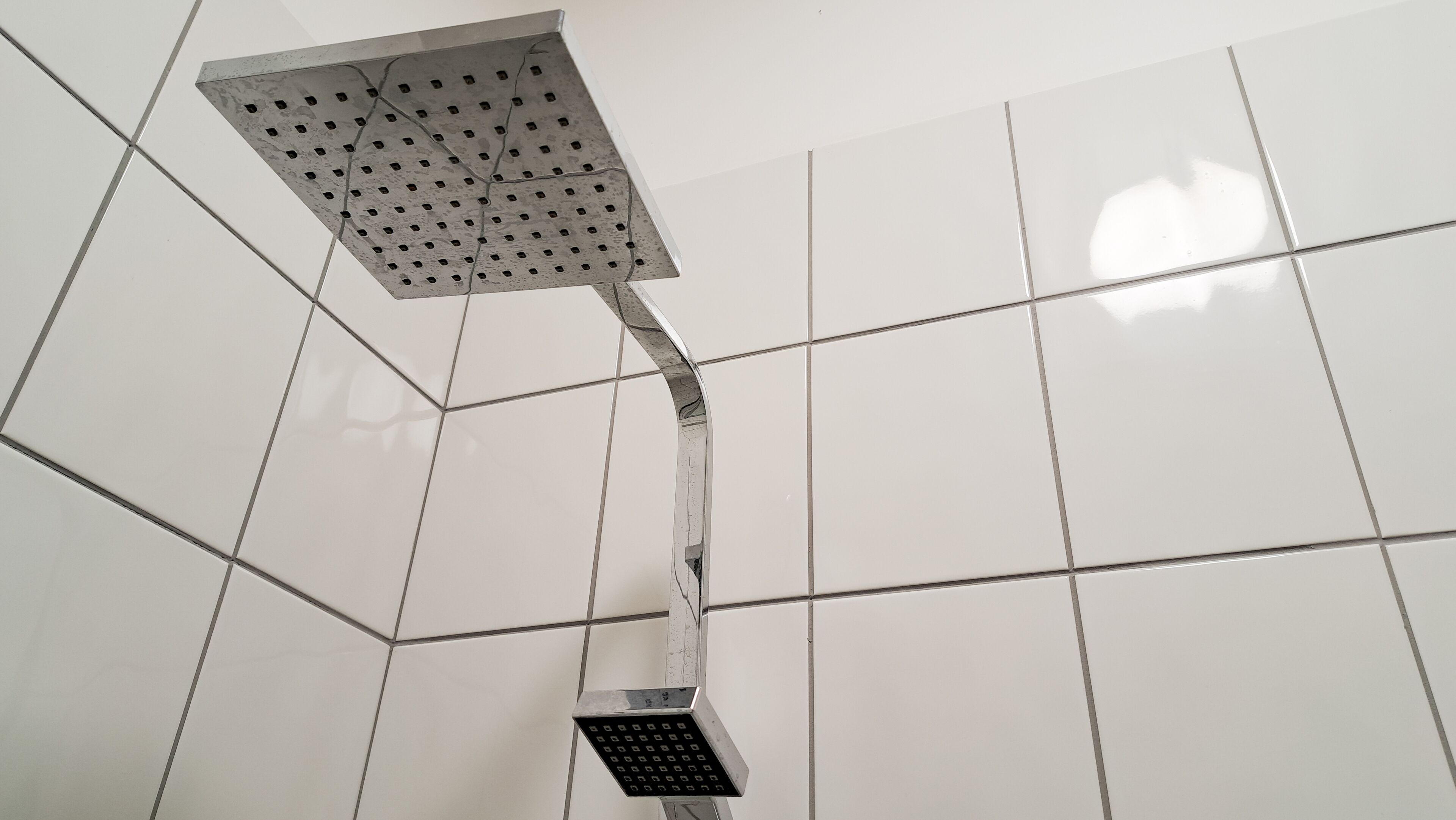 A showerhead with a square head and a curved handle, mounted on a tiled wall.