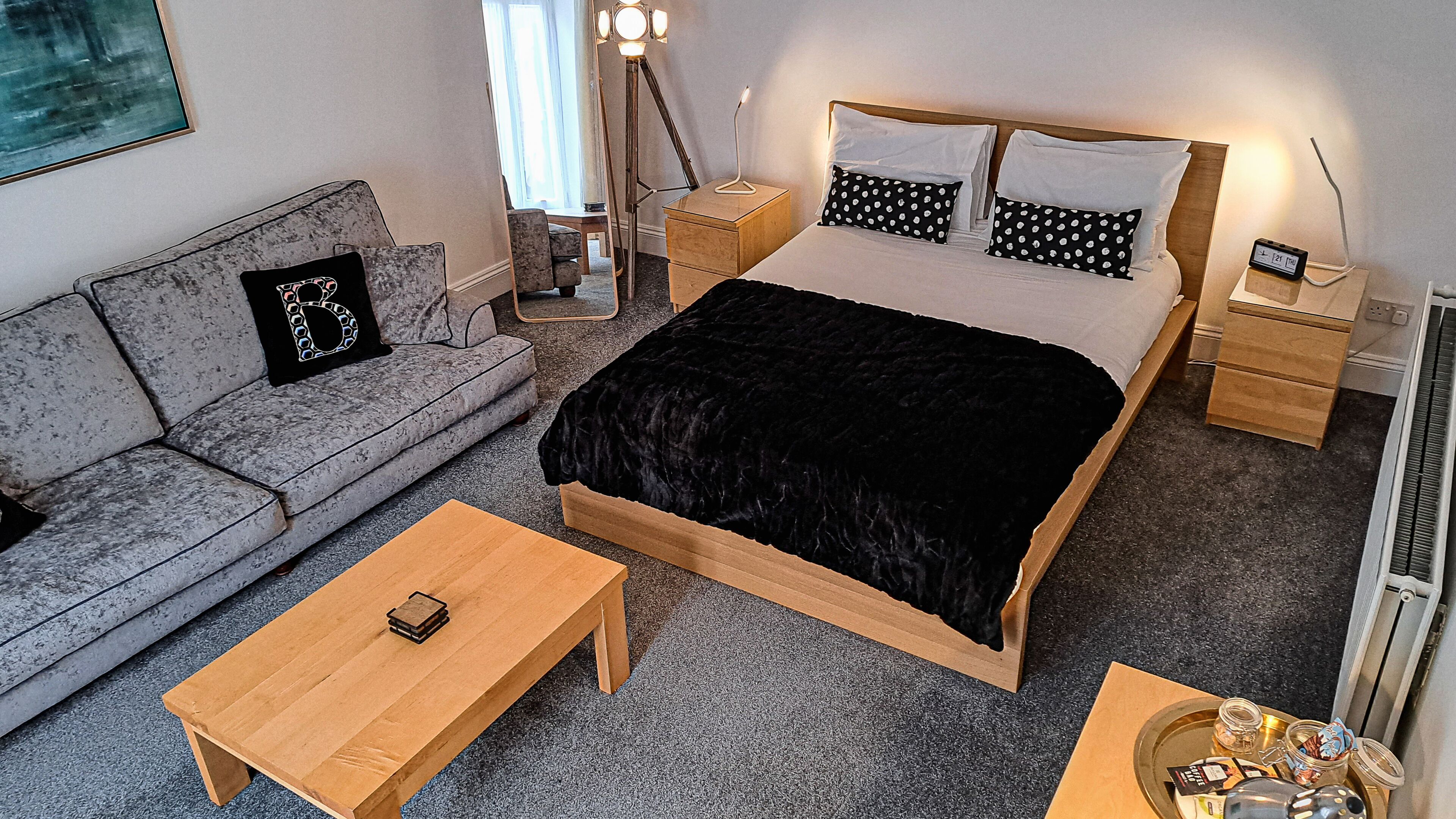 A bedroom with a bed, a sofa, a bedside table, a floor lamp, and a bedside clock.