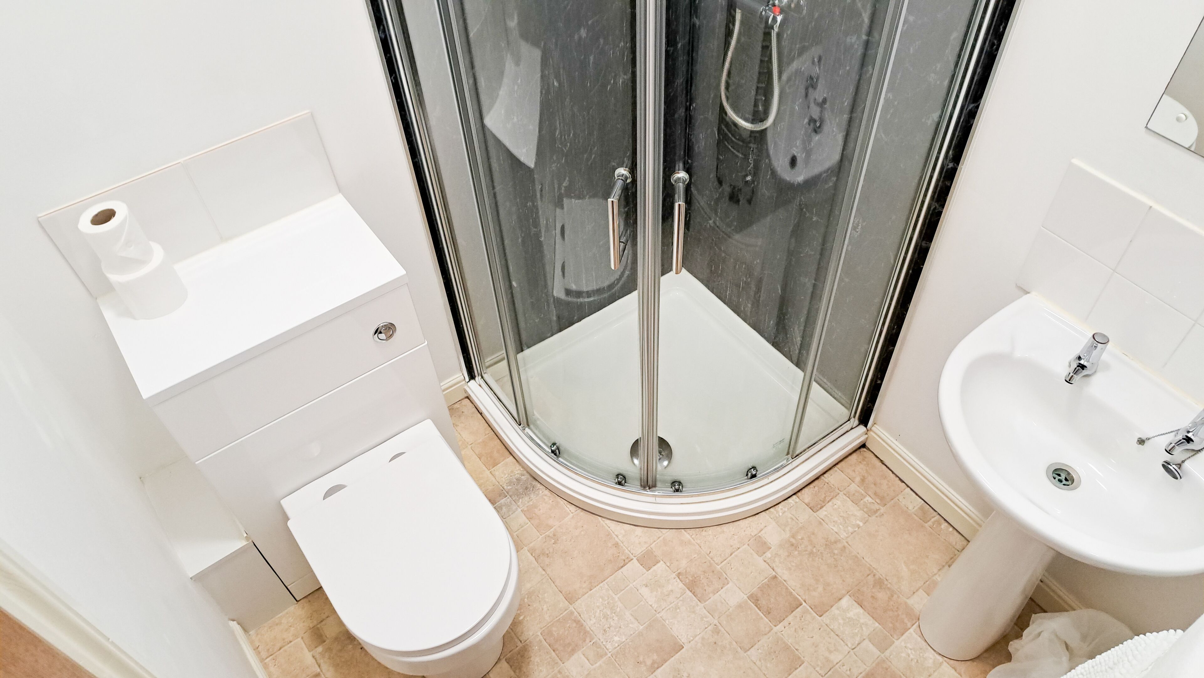 Een moderne badkamer met een douche met glazen wand, een toilet en een wastafel.