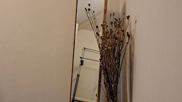 Une pièce d’angle avec un grand miroir, un vase blanc contenant des fleurs séchées et une moquette sombre.