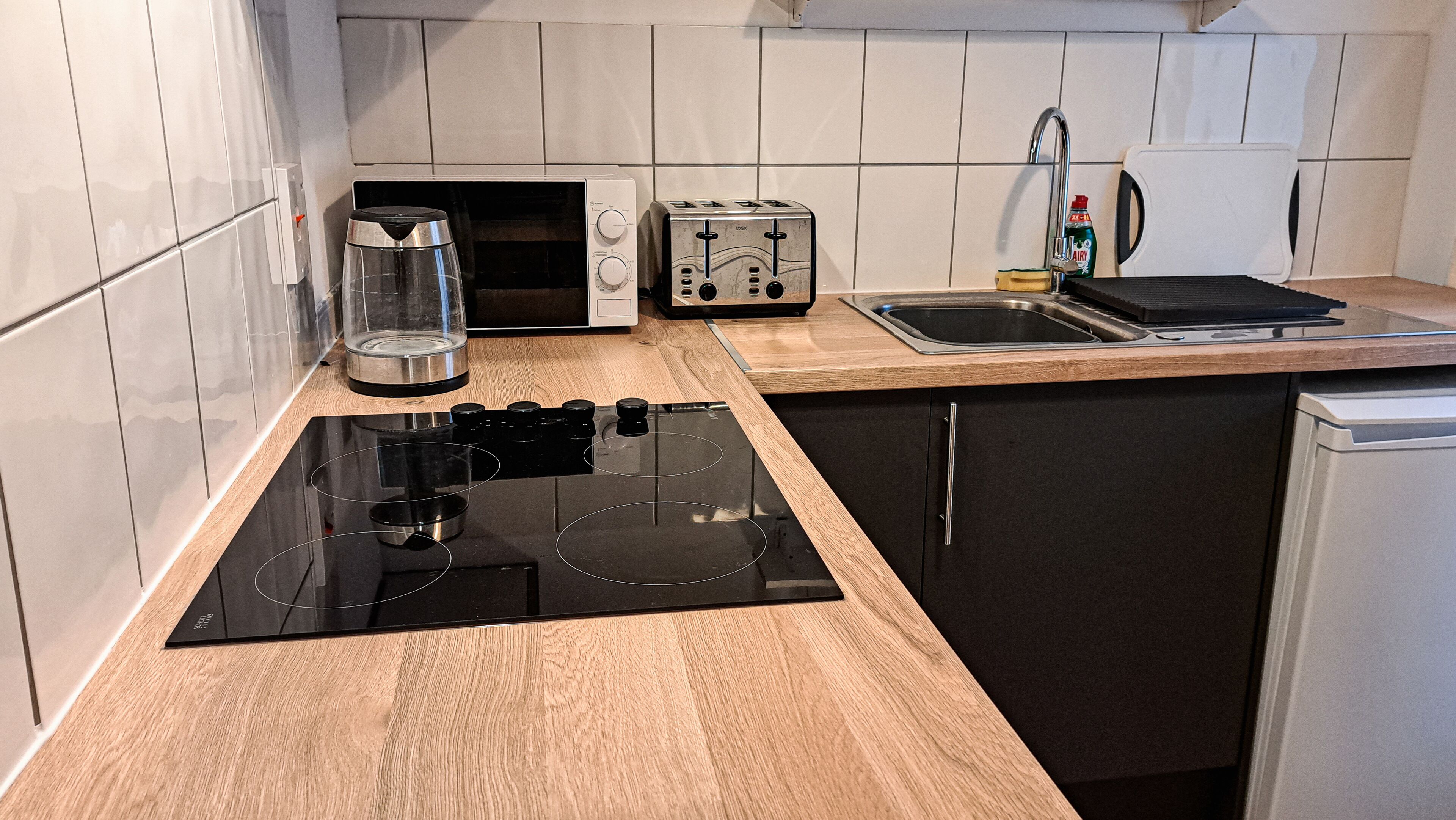 A modern kitchen with a black induction cooktop, a toaster, a kettle, and a sink.