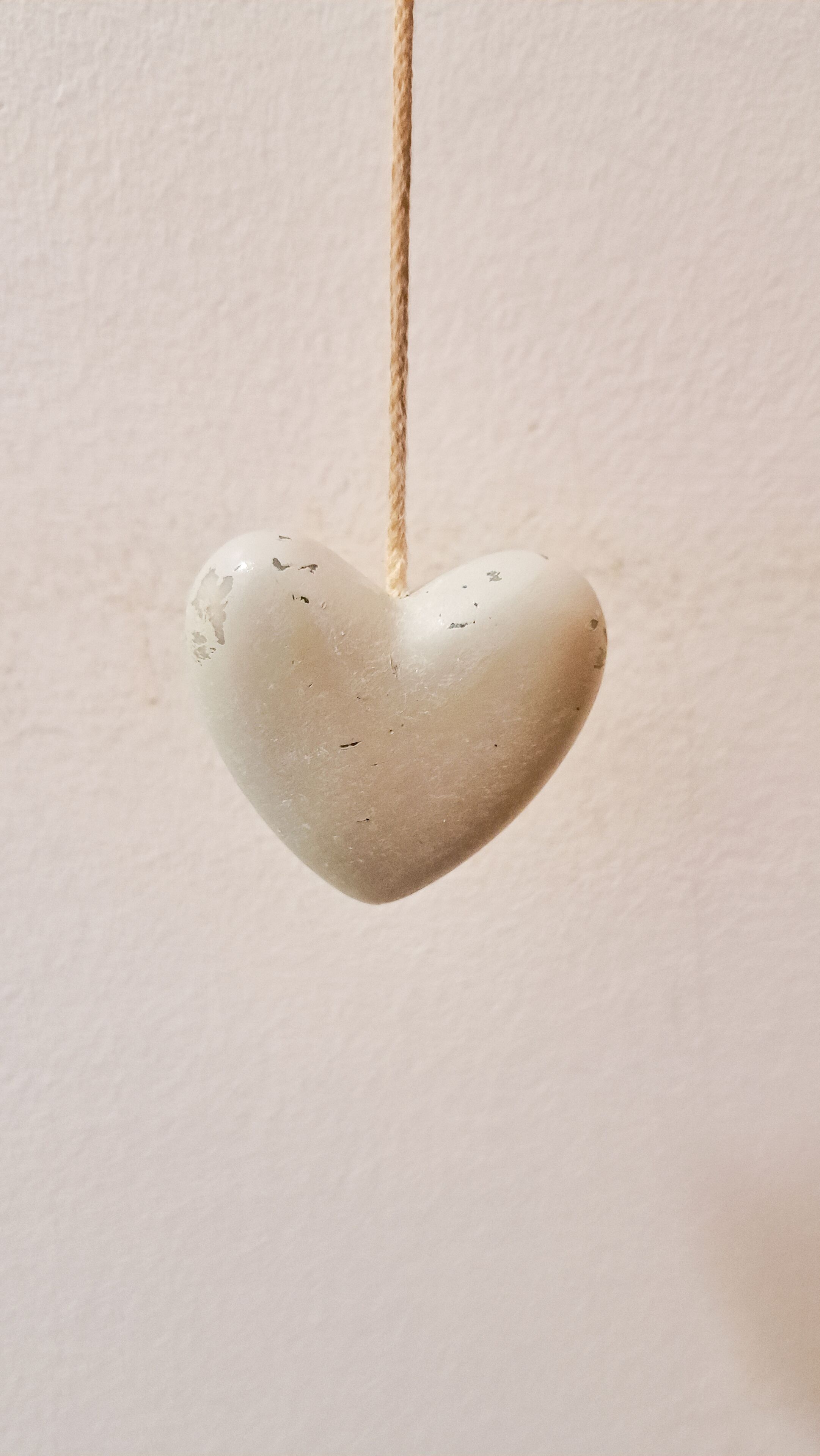 Un adorno con forma de corazón colgado de una cuerda frente a una pared lisa.