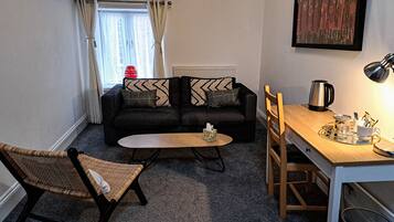 Un espacio habitable compacto con sofá, una mesita redonda pequeña, una silla, radiador y cafetera.