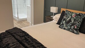 A bedroom with a bed, a nightstand, a lamp, a shower area, and a view of the outside. - The Old Vicarage (Northampton)