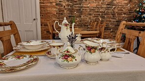 A dining table set with floral-patterned china, including bowls, cups, and a pitcher, against a brick wall backdrop. - The Old Vicarage (Northampton)