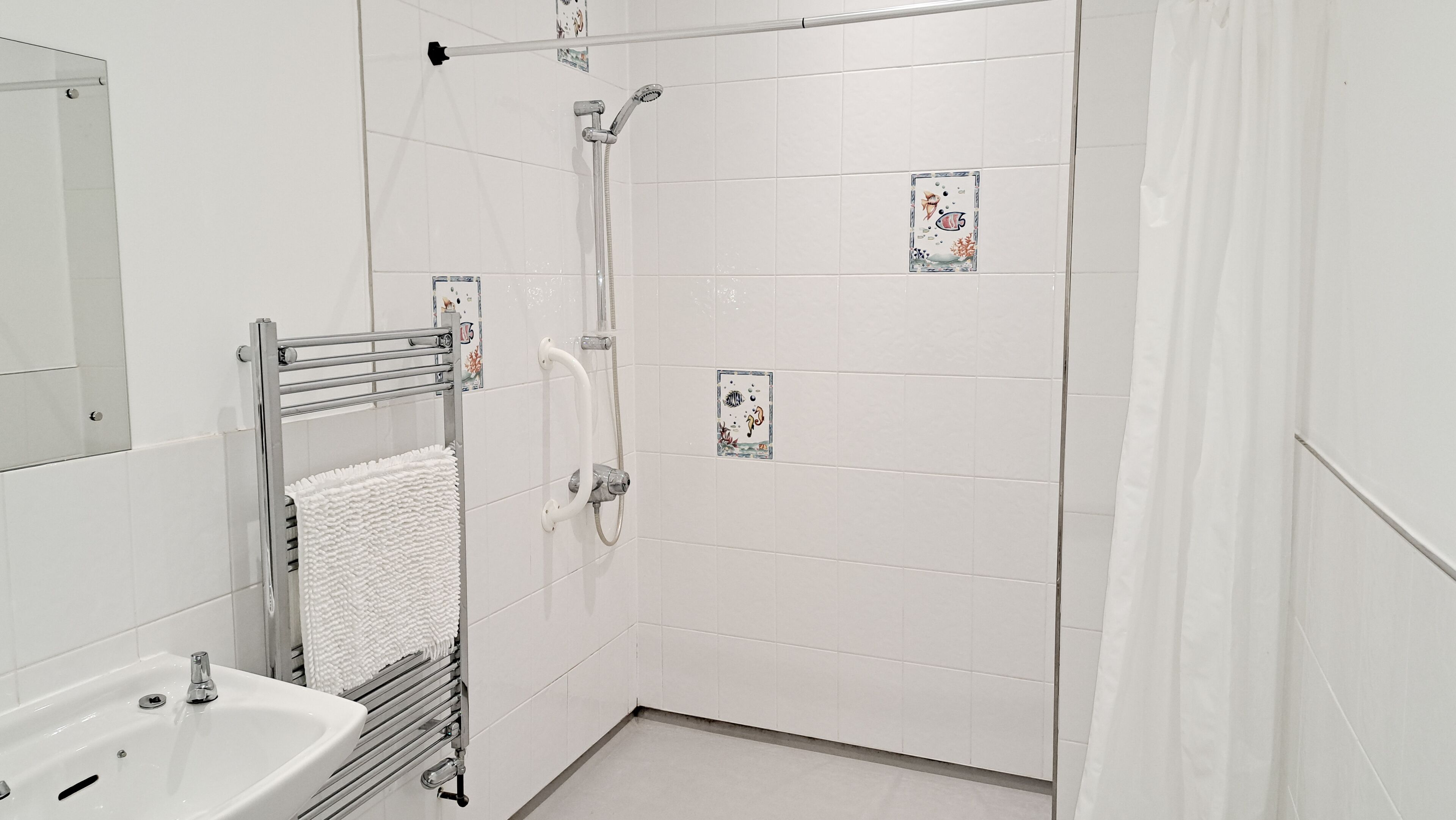 A modern bathroom with a shower, a towel rack with a white towel, a sink, and decorative tiles.