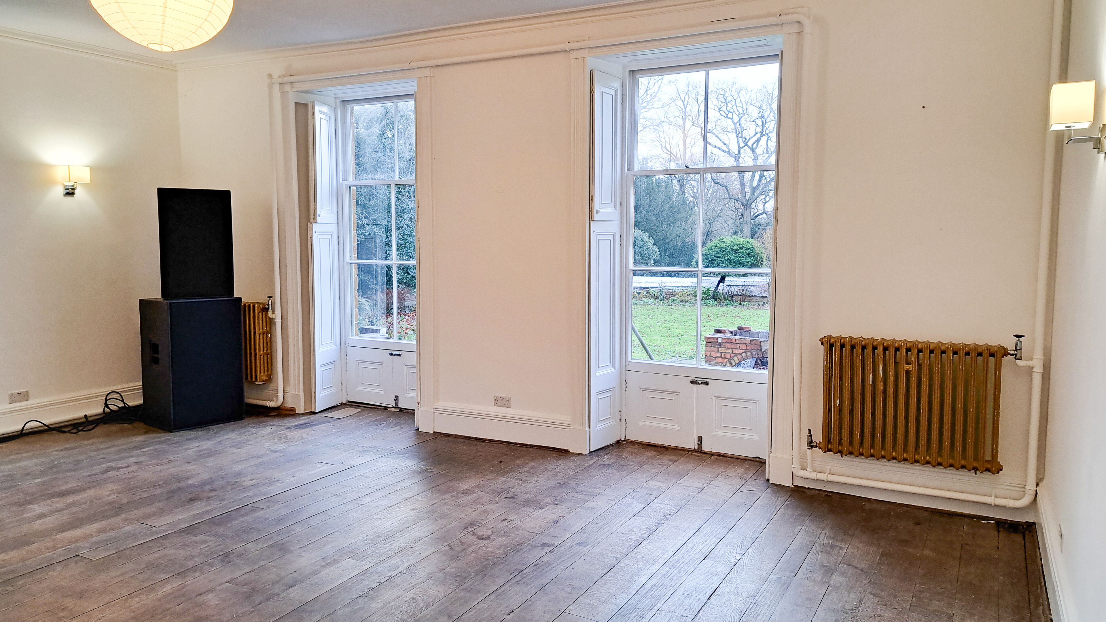 Une pièce avec un plancher en bois, deux portes blanches, un radiateur et un haut-parleur.