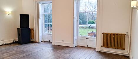 Une pièce avec un plancher en bois, deux portes blanches, un radiateur et un haut-parleur.