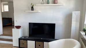 Un salon moderne avec un téléviseur à écran plat, un fauteuil blanc et des étagères décoratives.