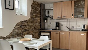 Une cuisine compacte avec un mur d’accent en pierre, des meubles blancs et un coin repas comprenant une table et des chaises blanches.