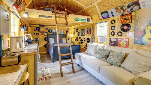 Ein Zimmer mit Holzboden, einer Himmelsleiter, einer Couch, einem Schreibtisch und Wanddekorationen, darunter Schallplatten.